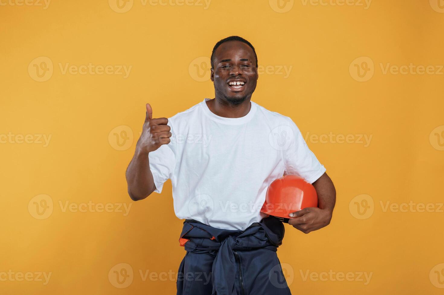 Holding, hard hat in hand. Handsome black man is in the studio against yellow background photo