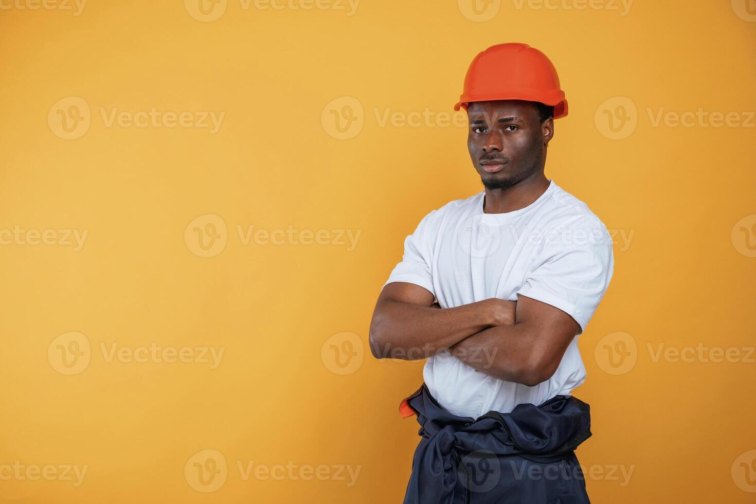 In, orange hard hat. Construction worker. Handsome black man is in the studio against yellow background photo