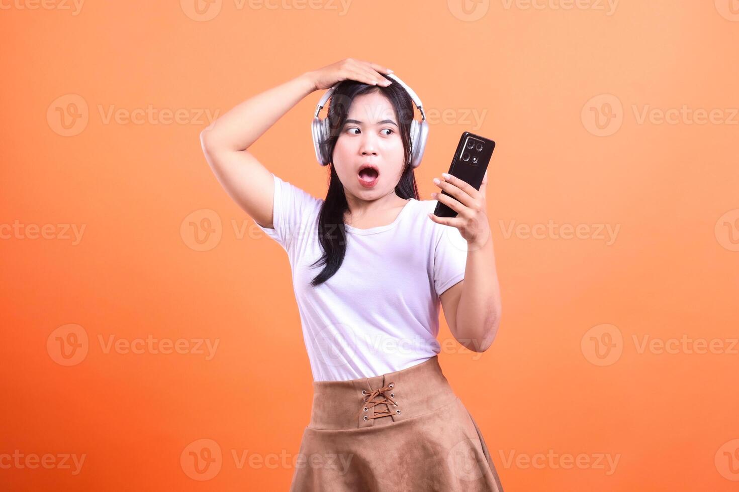 Surprised woman with headphones and phone isolated on orange background photo