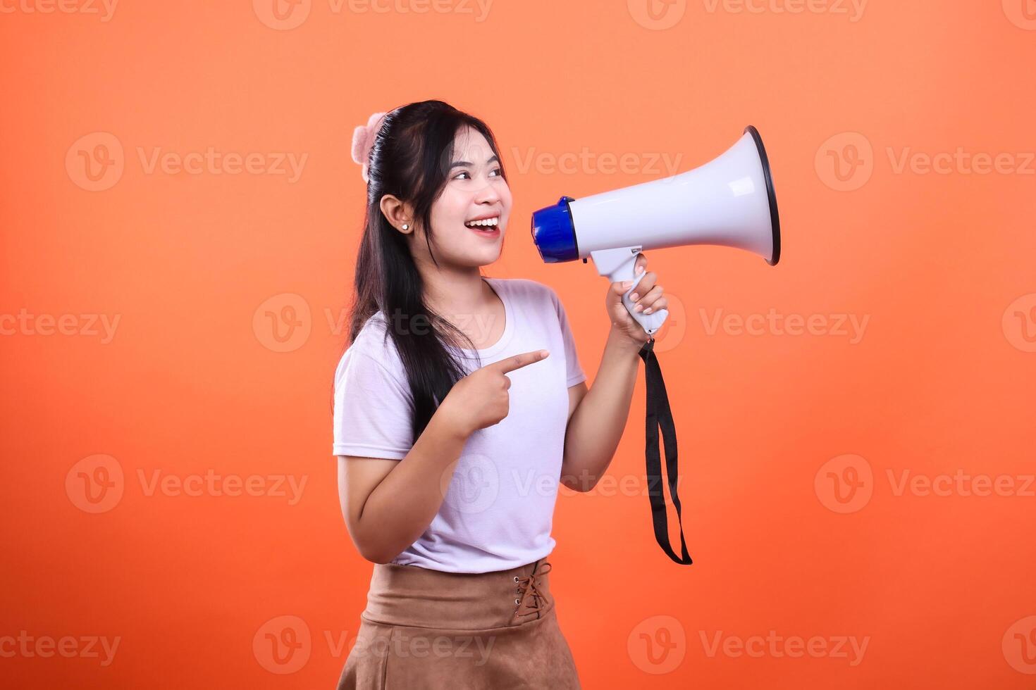 Young woman holding a megaphone and pointing with her index finger isolated on an orange background photo