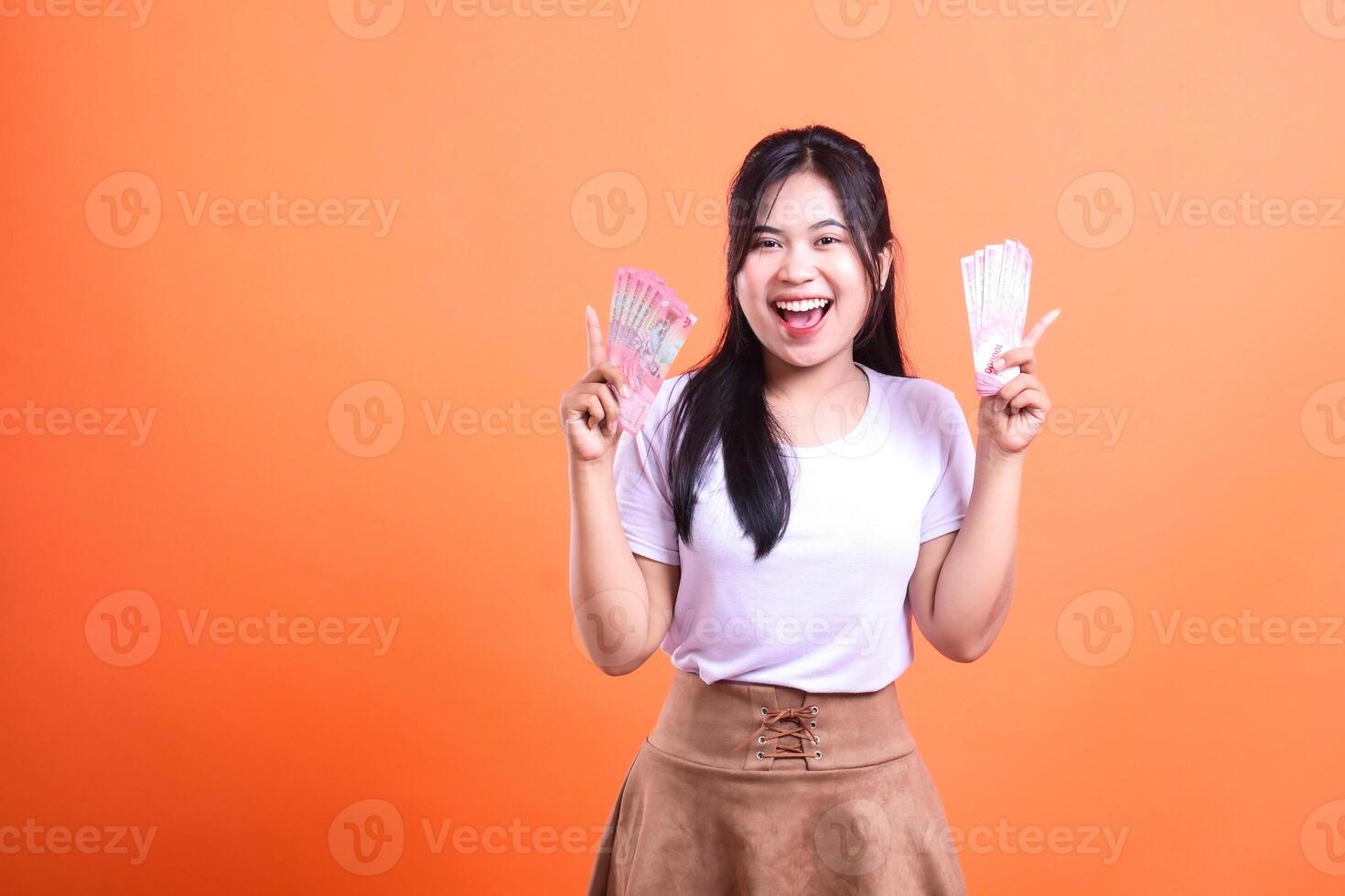Young woman smiling holding money in both hands on orange background with copy space photo