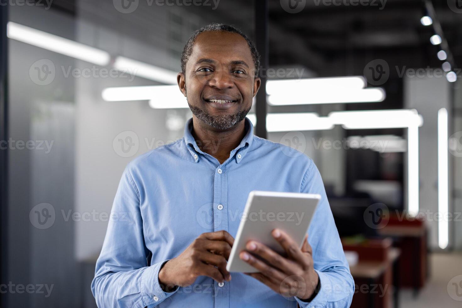 Mature african american businessman using digital tablet in modern office. Confident expression, business professionalism, and technology highlight his expertise. Ideal for business or tech themes. photo