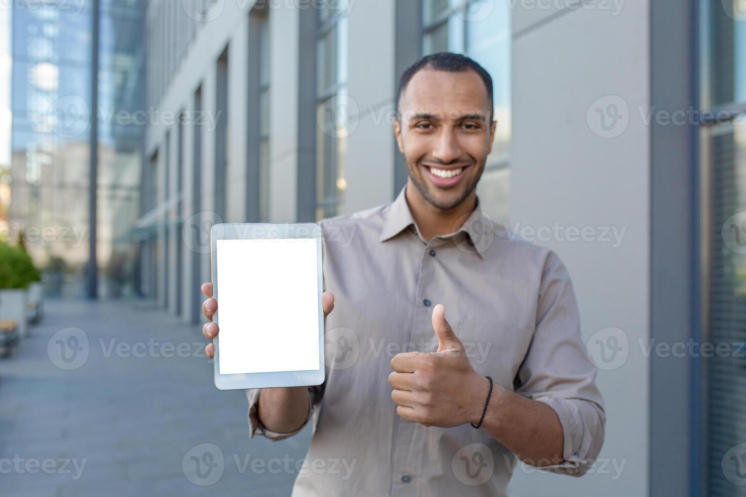 Satisfied arab male making thumb up gesture while holding digital tablet with blank screen on urban background. Modern device user recommending and approving new useful commercial application. photo