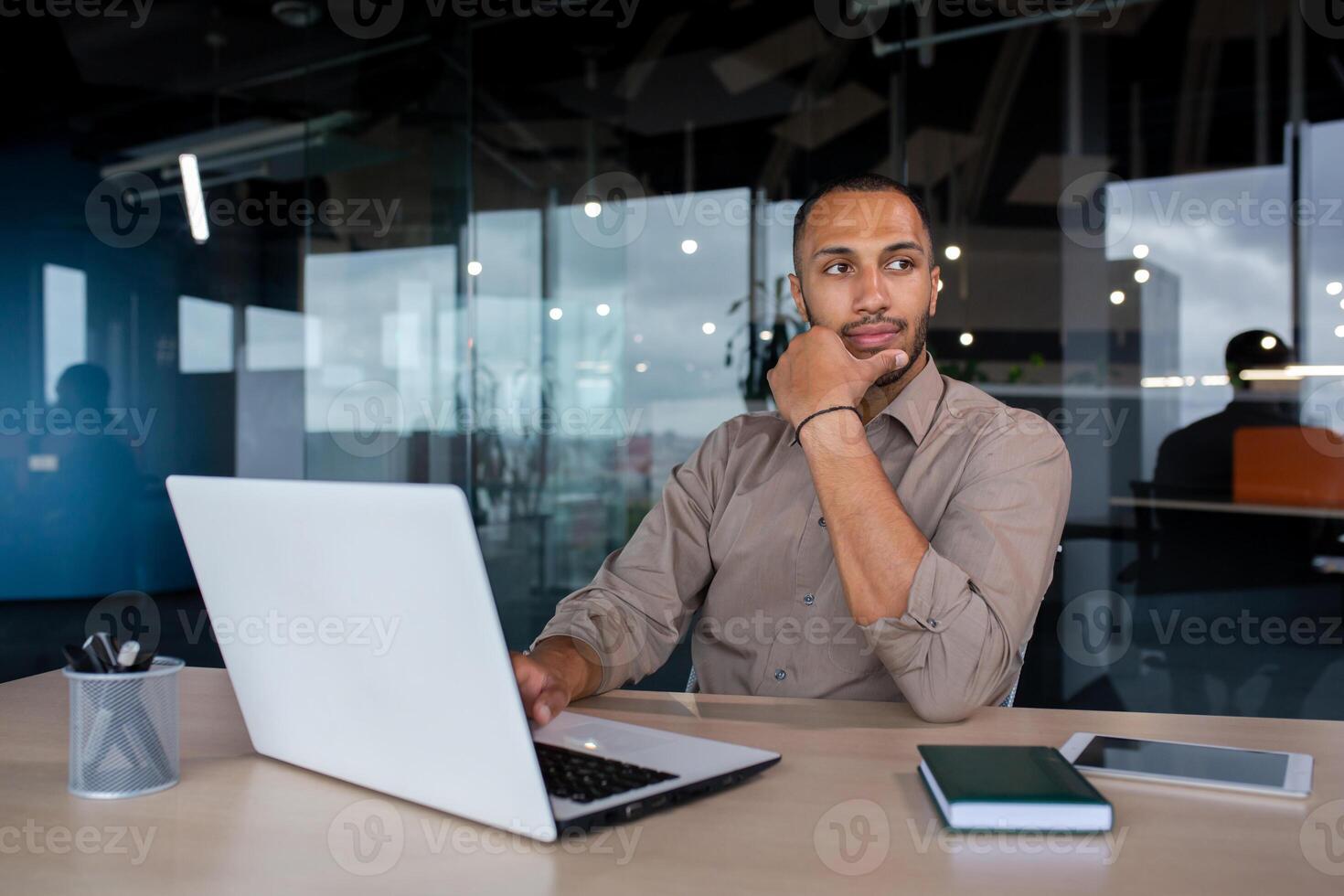 Focused serious thinking businessman at workplace inside office, man thinking about financial technical solutions working with laptop. photo
