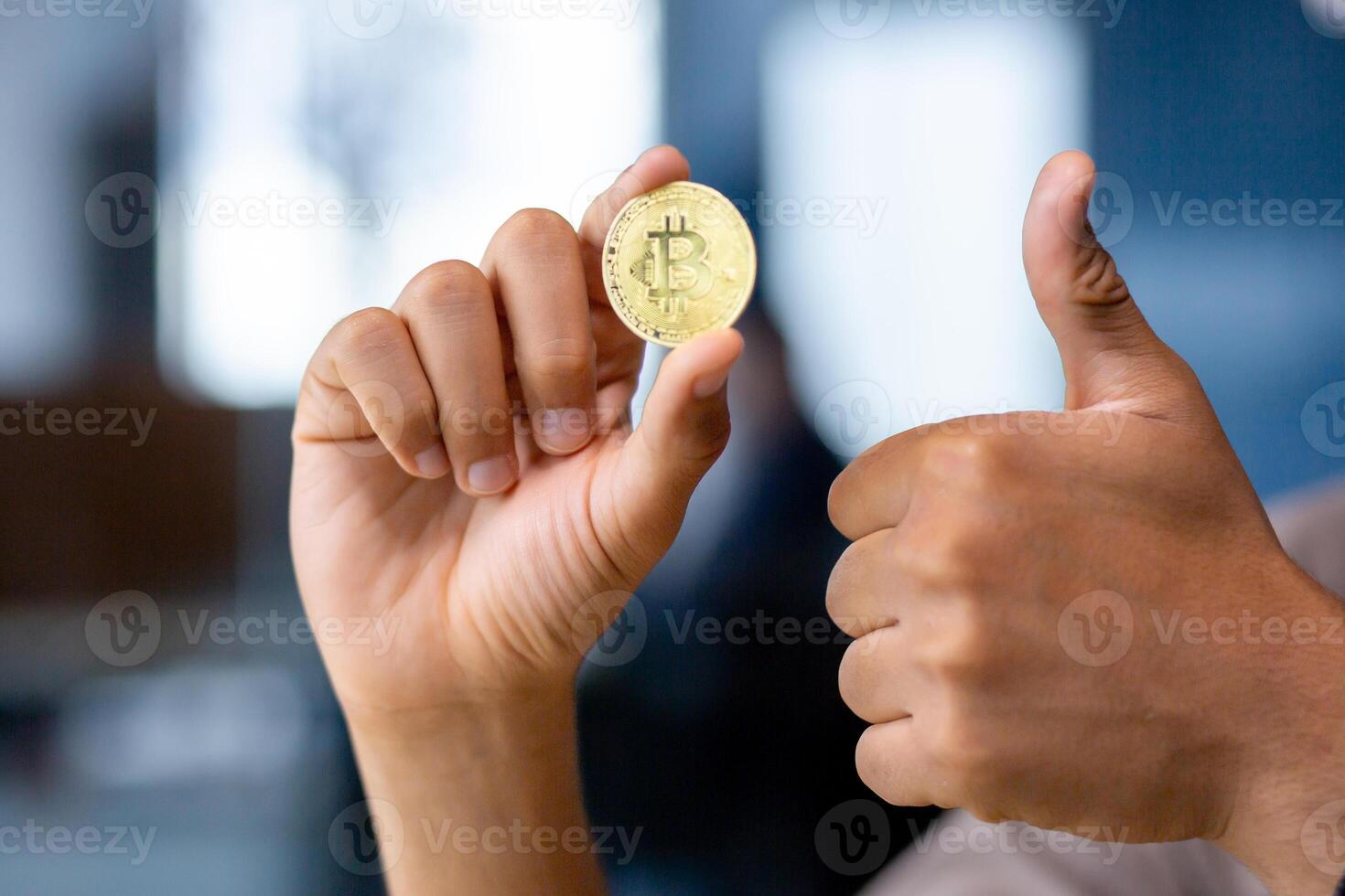 Close-up portrait of hands holding bitcoin virtual currency and showing like thumbs up, office space. photo