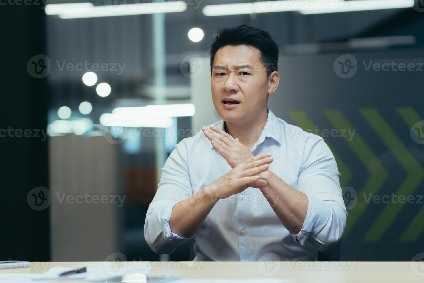 Angry asian businessman talking on call online meeting, looking at web camera, gesticulating angrily with hands, man at work in office photo
