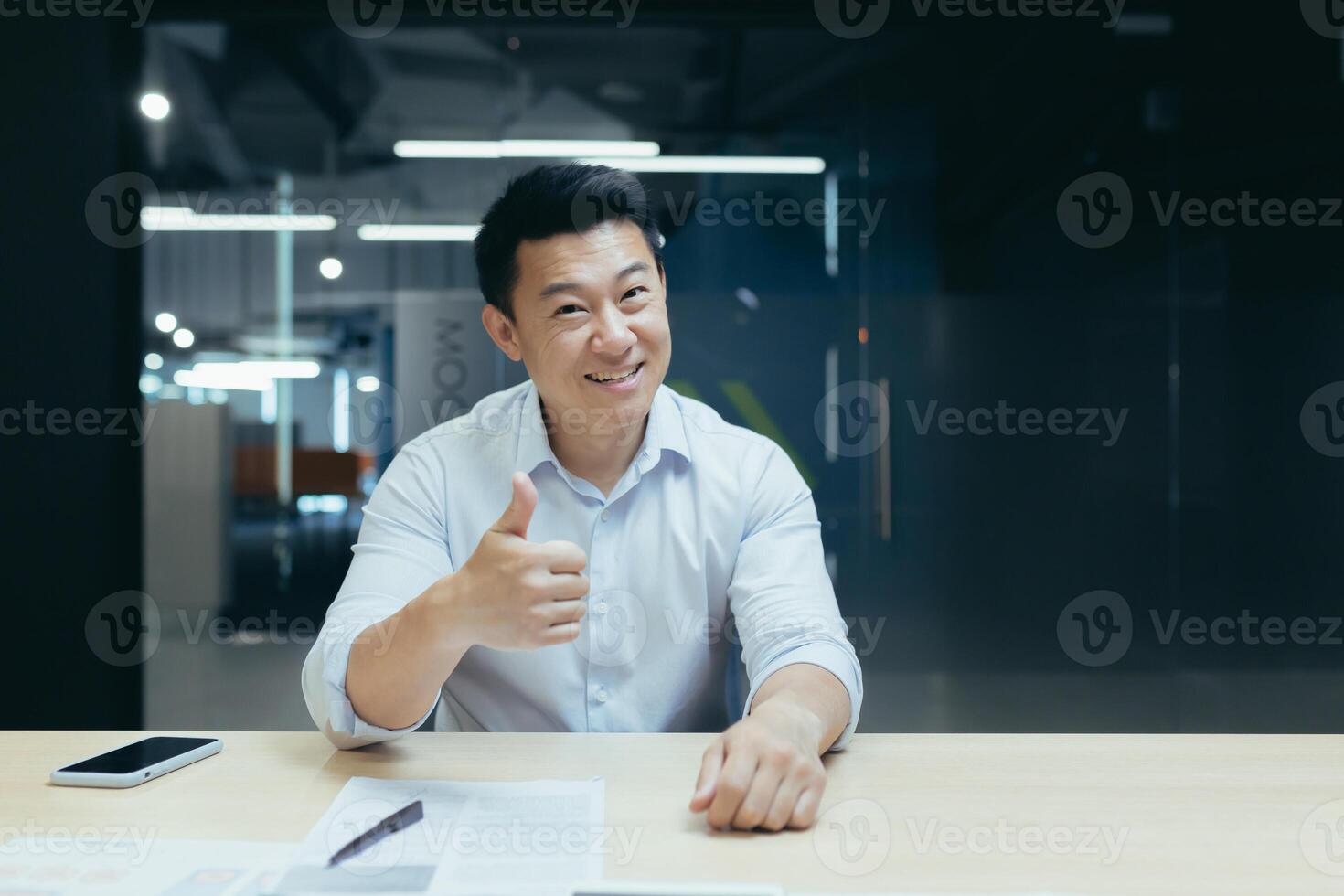 Portrait of successful asian businessman man smiling and looking at camera, boss holding thumbs up approvingly, call and online meeting photo