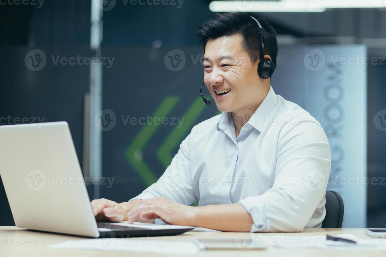Learning online. Young handsome male Asian student studying remotely with laptop and headphones. Sitting at a desk in an office on campus. photo