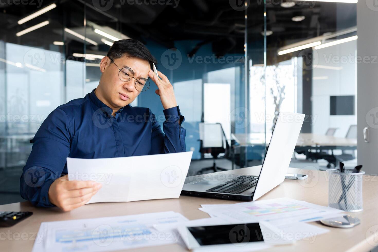 Desperate businessman looks and reads financial reports and documents, Asian boss works with documents inside office, confused and depressed. photo