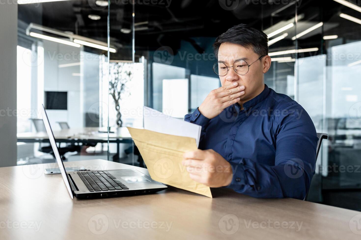 Disappointed Asian man received letter, man reading bad message, businessman working inside modern office building. photo