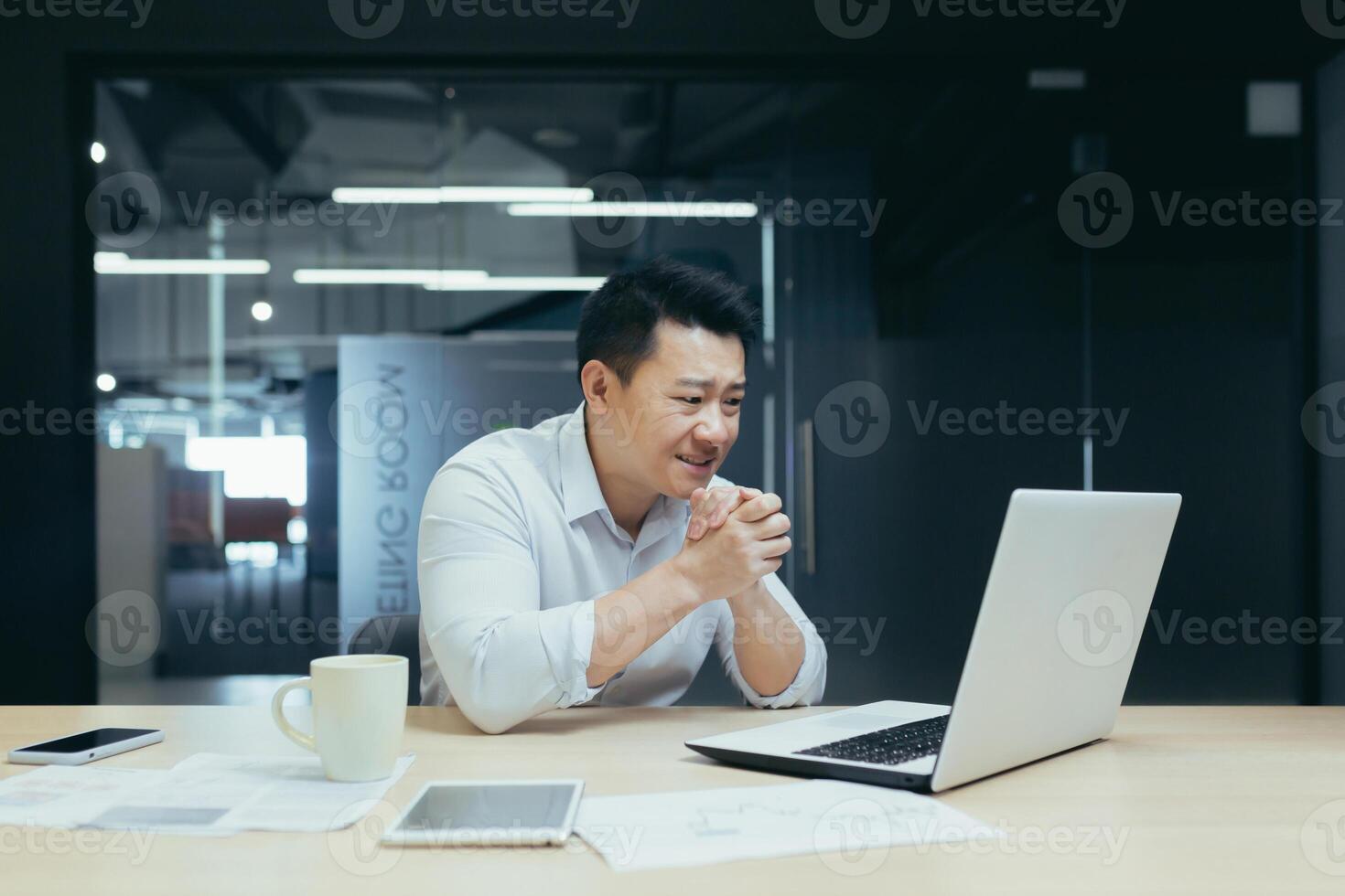 Young handsome male Asian freelancer conducts a meeting on a call from a laptop. Sitting at the table in a modern office, smiling, talking. photo
