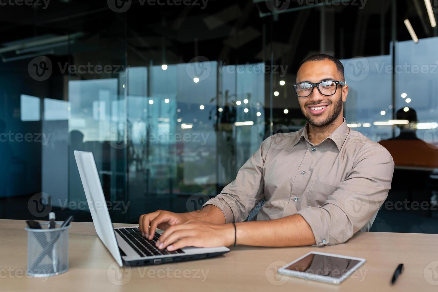 Portrait of successful hispanic businessman inside office, man with laptop working typing on keyboard smiling and looking at camera. photo