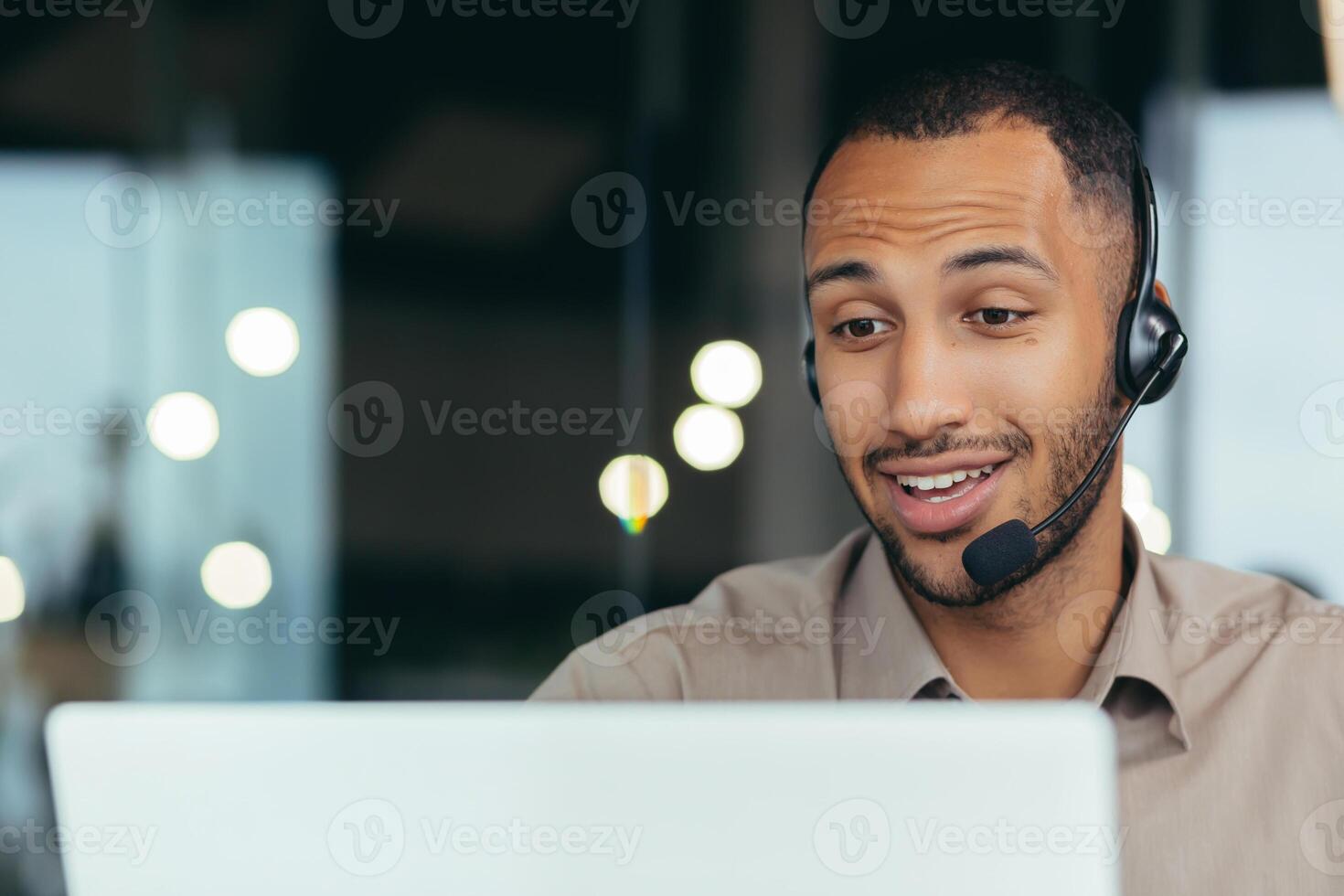 Close-up photo. Learning online. A young handsome African-American student is studying remotely from a laptop, sitting at a desk in a headset, talking on a call. photo