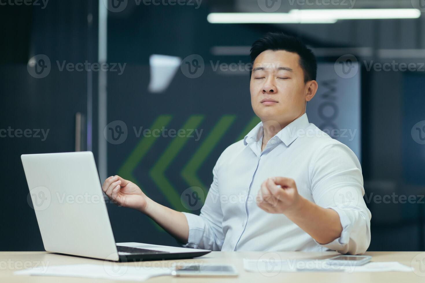 Portrait of Asian businessman, man in office working with laptop, meditating at workplace with eyes closed photo