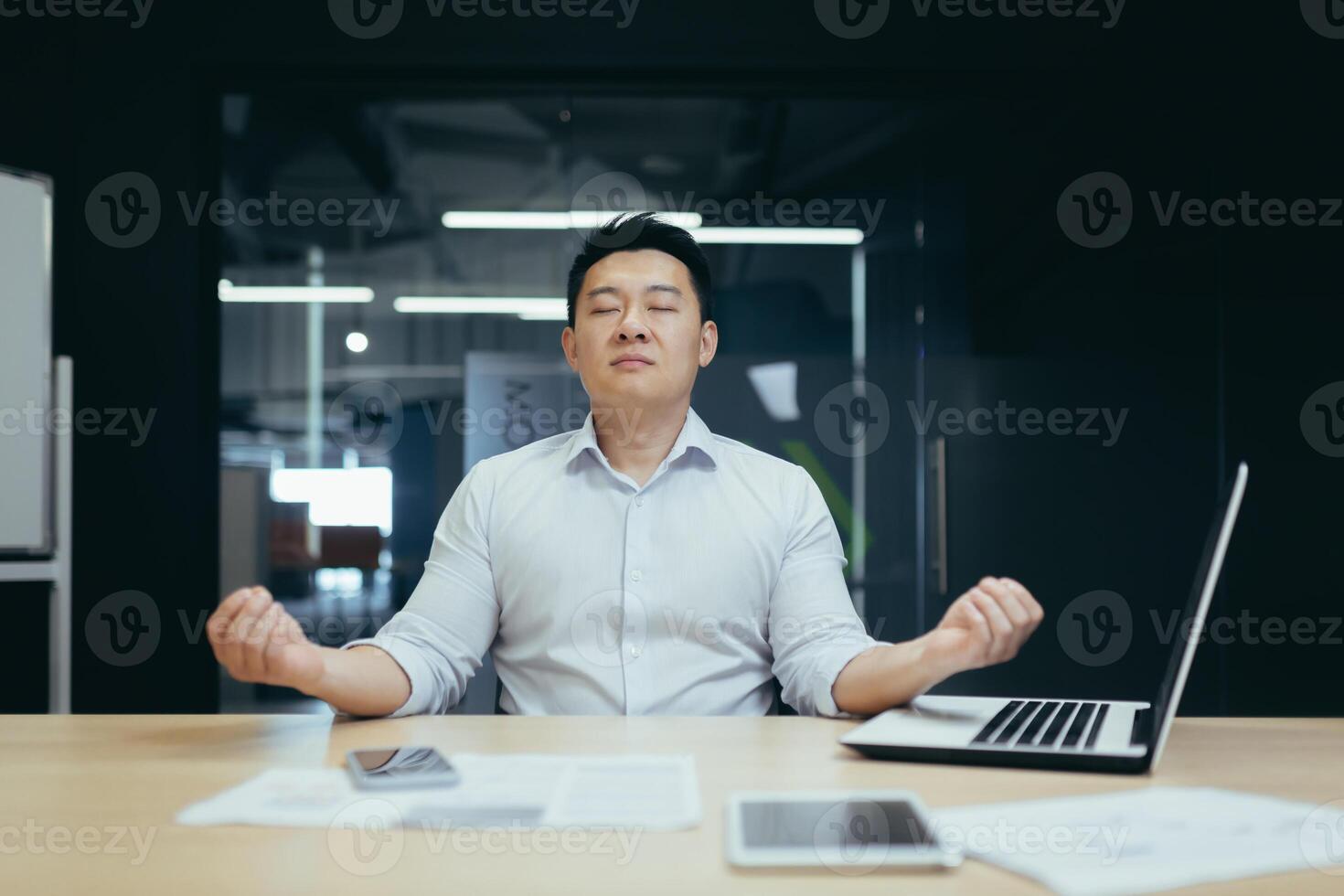 A break at work. Handsome young Asian businessman man meditating at the workplace in the office, closed his eyes, holds his hands in the lotus position, rests, relaxes. photo