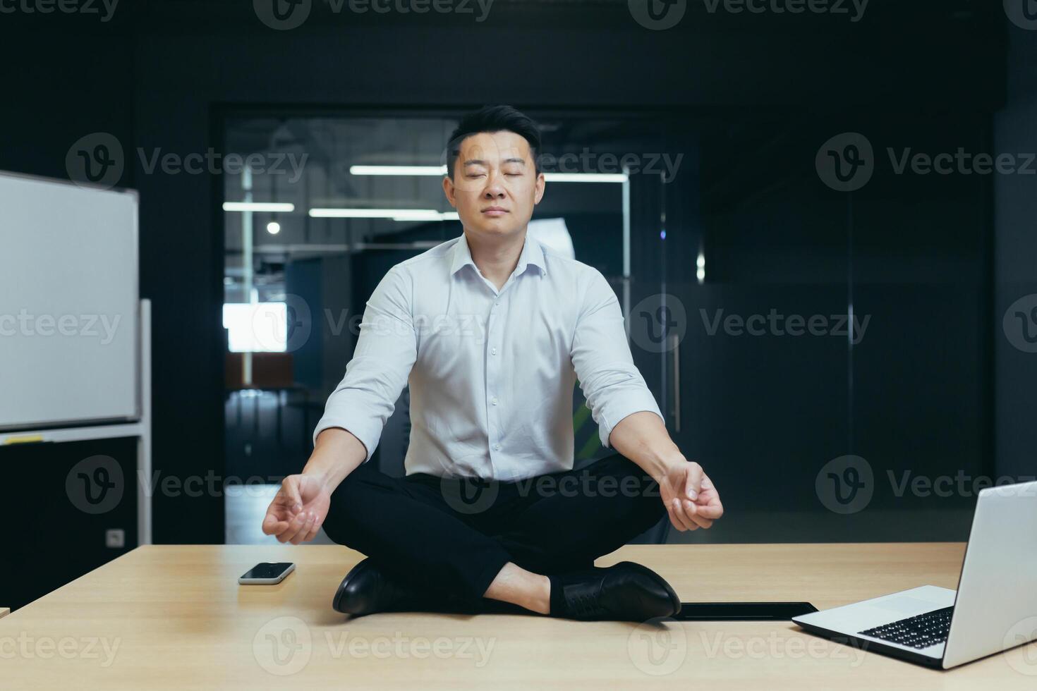 Asian boss businessman meditating in office, man sitting in lotus position on desk with closed eyes, thinking about important decision photo