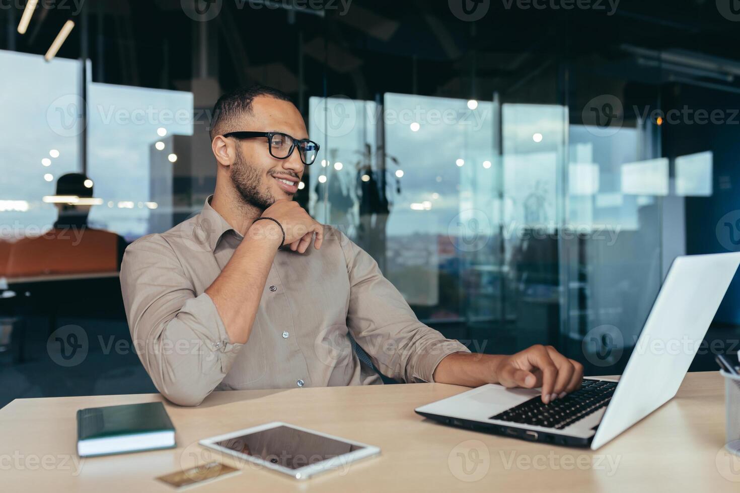Happy and successful Indian man working in modern office building, programmer in glasses using laptop to write code, businessman in shirt smiling and happy . photo