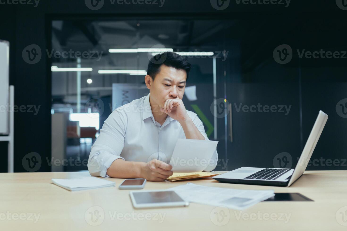 Stressed young asian businessman working from office report annoyed with low sales. Nervous boss see c mistake incorrect information in paper document photo