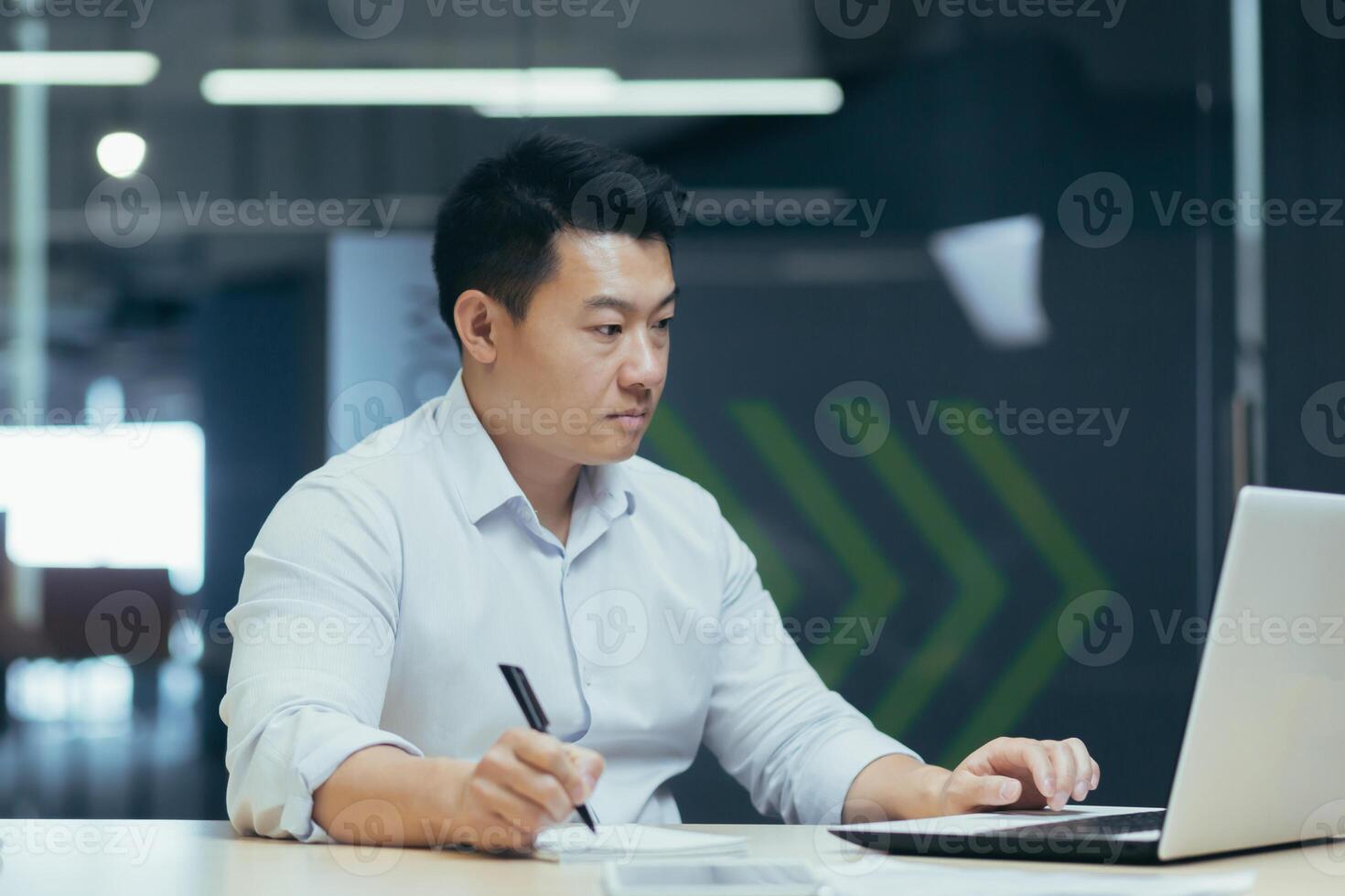 Serious and focused asian male accountant working with documents in modern office, businessman behind paper work photo