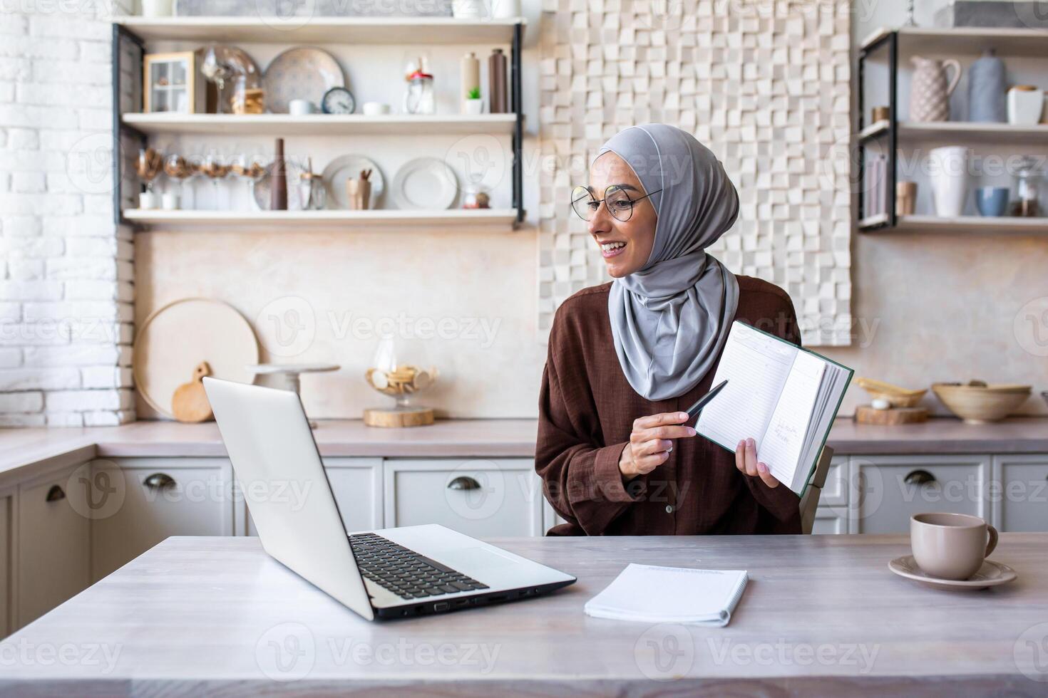 Online training. A young Muslim woman in a hijab teaches at home remotely via zoom from a laptop. Shows the camera a book, a notebook, explains, reads a lecture. photo
