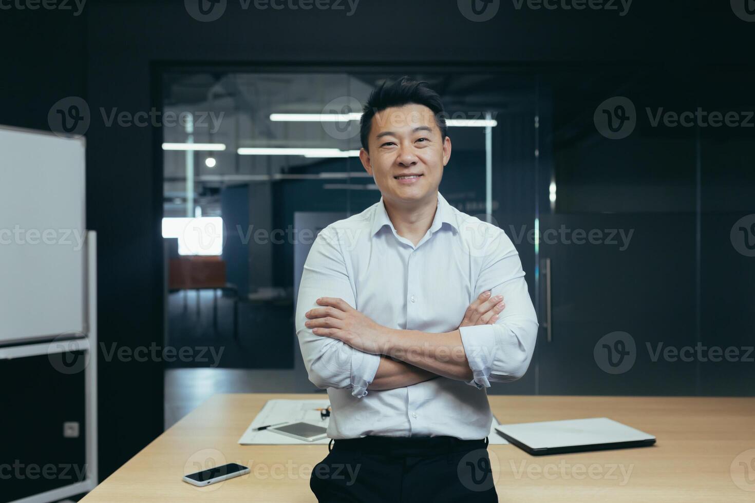 Portrait of successful asian boss in modern office, man standing with crossed arms smiling and looking at camera, portrait of successful businessman investor photo