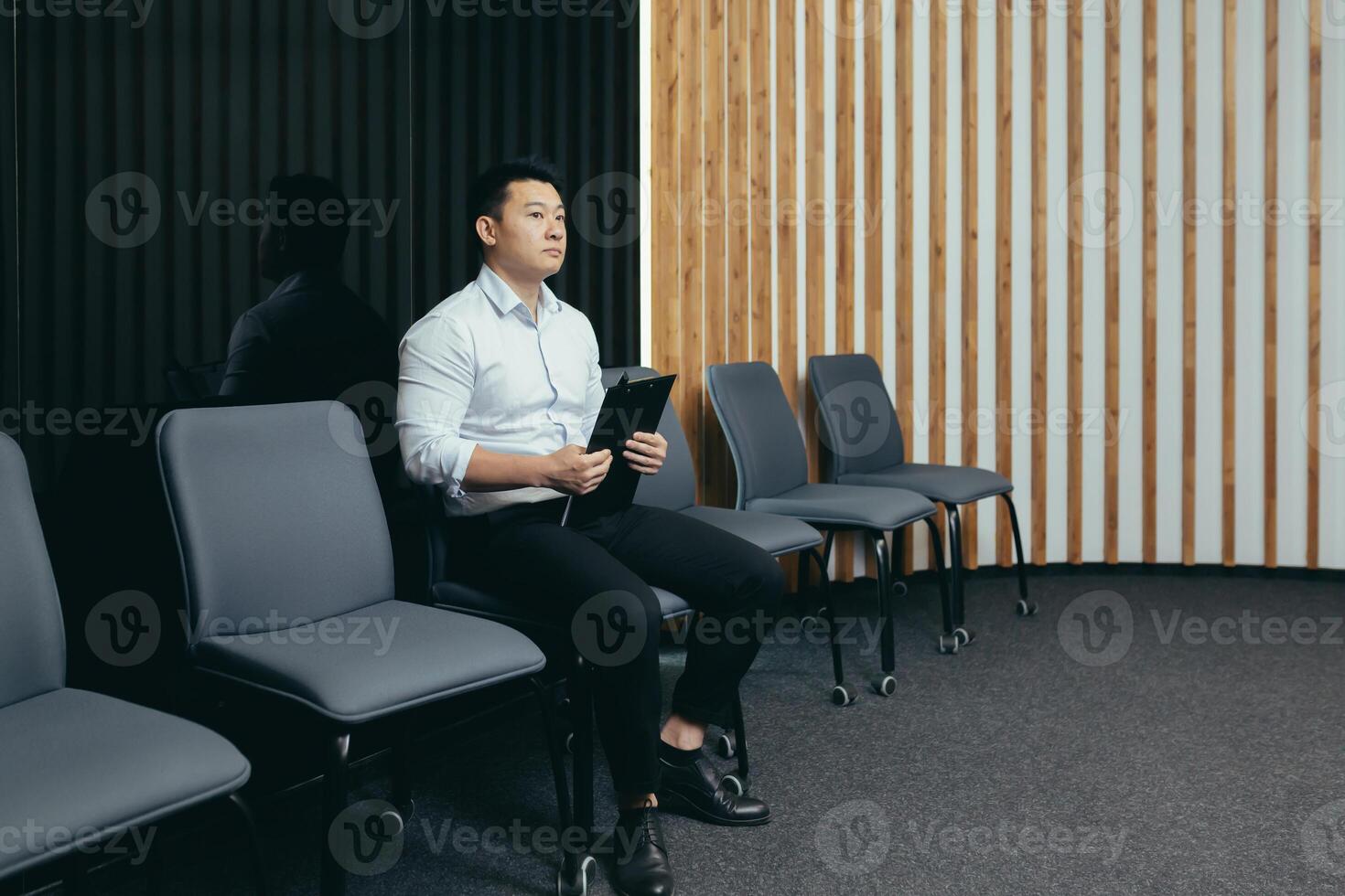 A young handsome Asian man is waiting in the reception hall for an interview for a job in an office, bank, business company. He holds a folder in his hands, worries, shakes it off photo