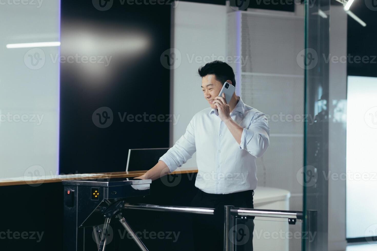 The worker enters the office, opens the door with an electronic key with a card, an Asian man smiles and talks on the phone photo