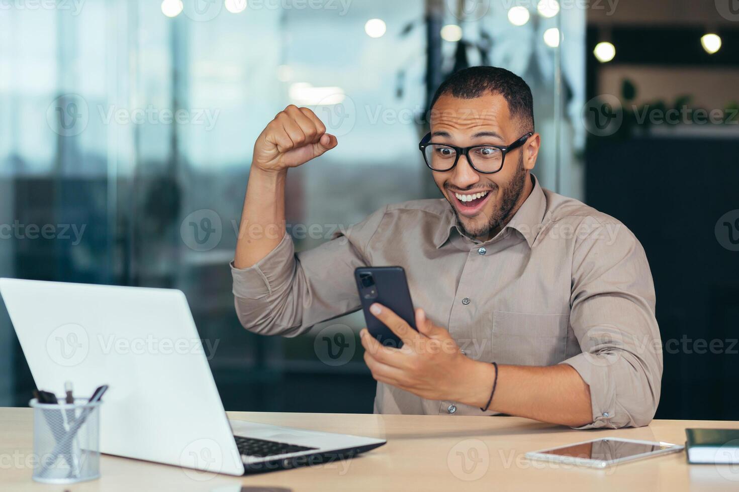Successful african american businessman working inside modern office building, man celebrating victory and success received good news online notification phone, investor in happy with work result. photo
