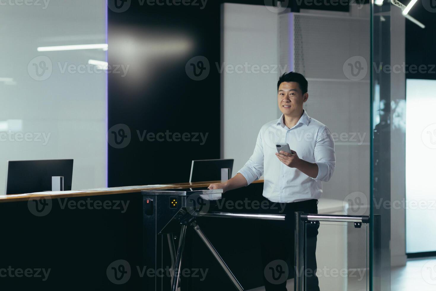 A young handsome Asian businessman, an office worker goes to the office and the business center for work in the morning through the security counter and automatic electronic pass. He holds the phone photo