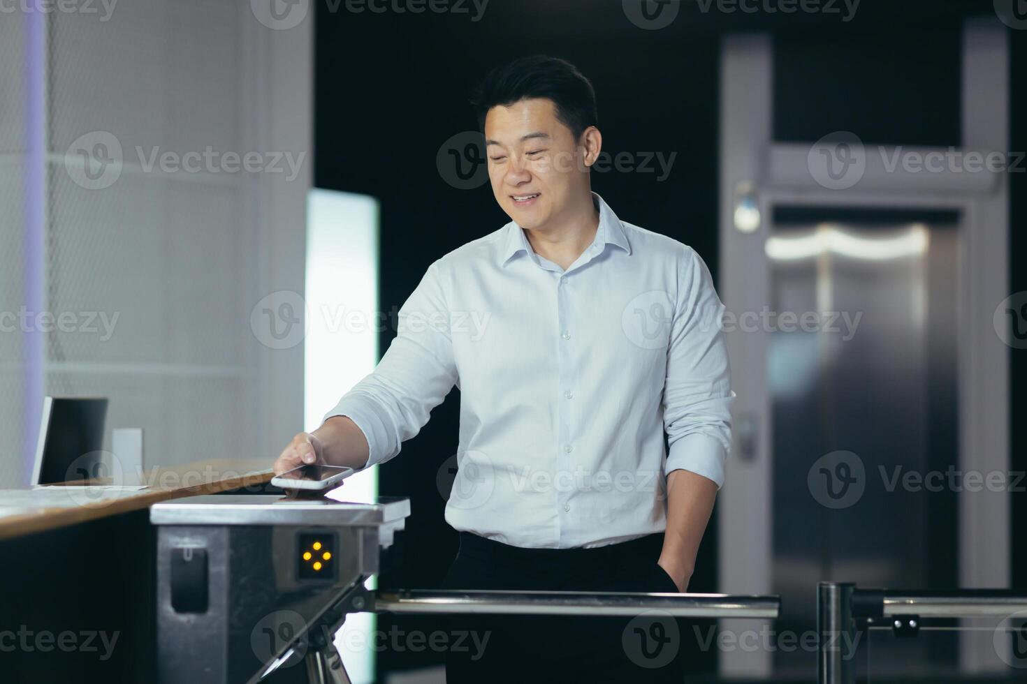 A young Asian businessman enters a modern office center through electronic automatic turnstiles, puts his phone to open and read the code by the system, keeps his hand in his pocket. photo