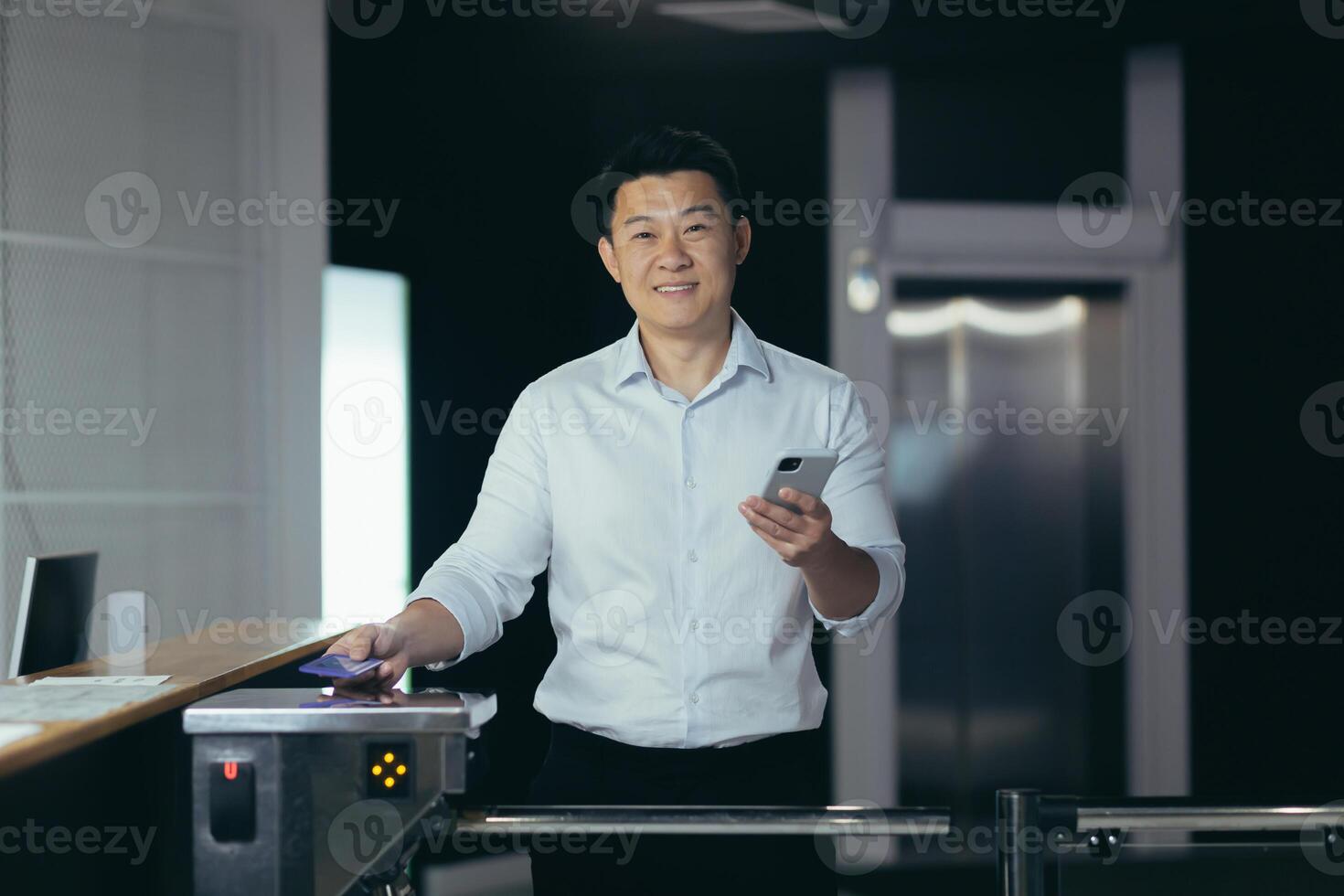 Portrait of an Asian businessman worker, man comes to work for the first time, walks into the office, smiles and looks at the camera at the front door, holds a phone in his hands photo