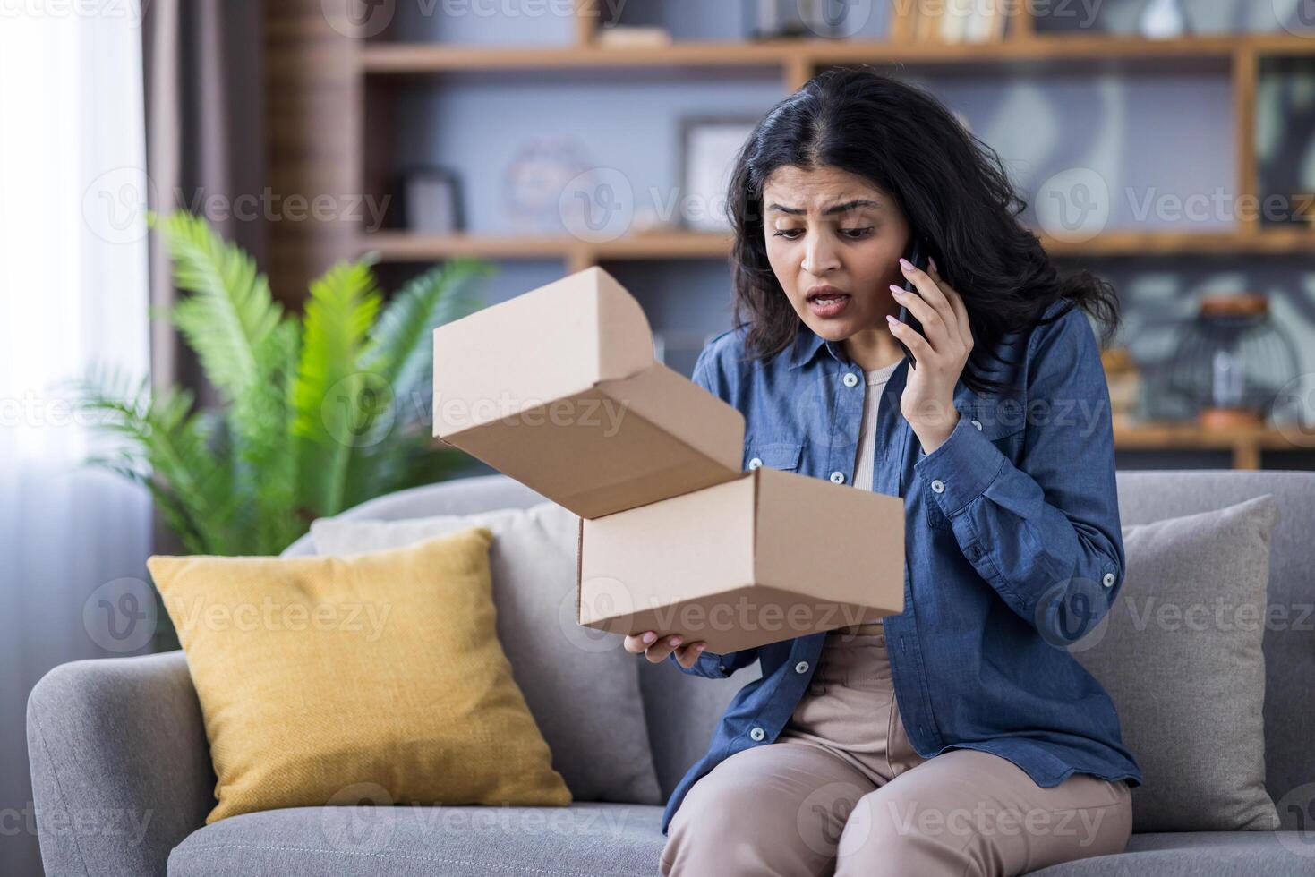 A young woman looks shocked as she opens a cardboard package, immediately calling customer service to report the issue at her home. photo