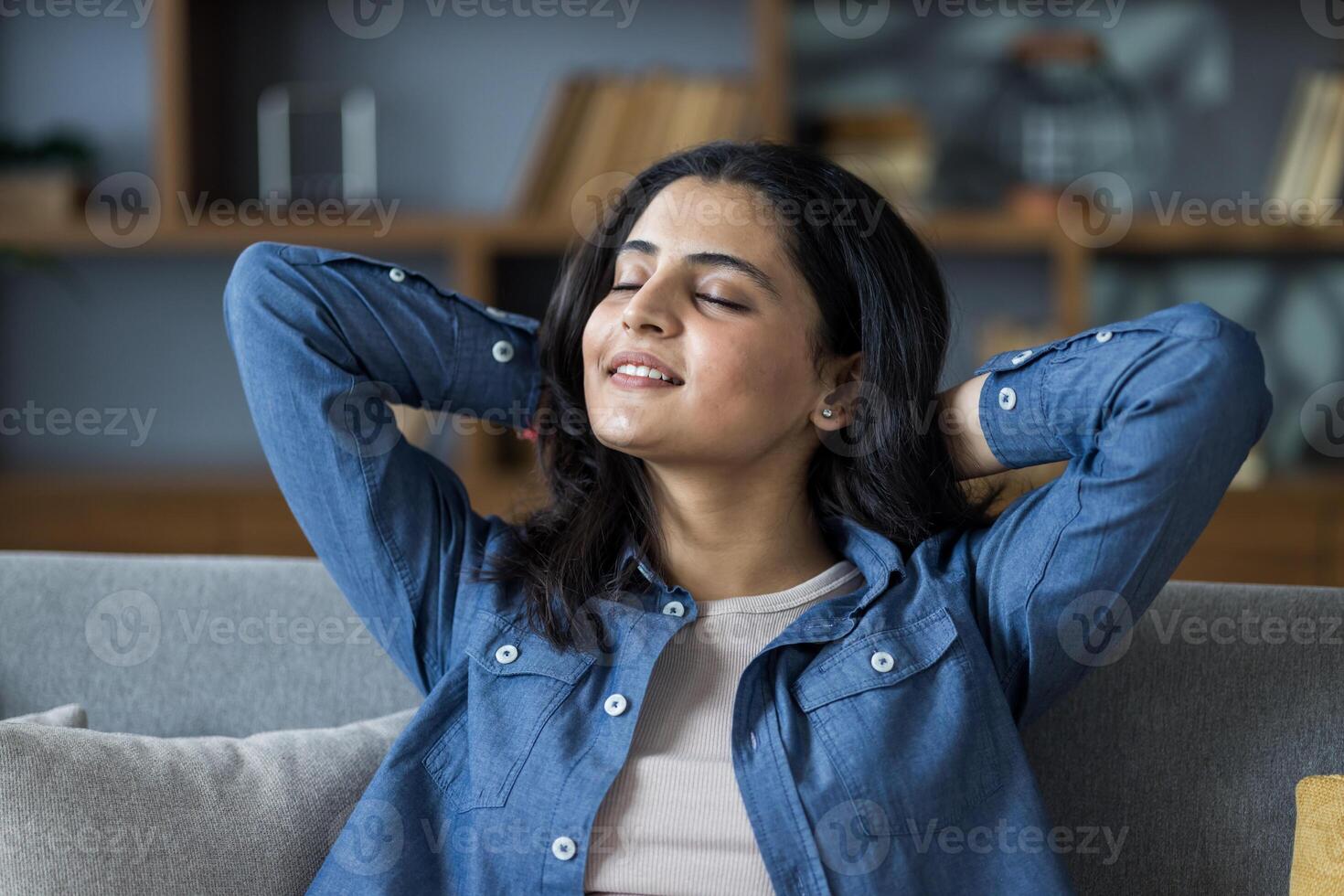Woman relaxing on the sofa with her hands behind her head and eyes closed, enjoying the peace and quiet of her home. photo