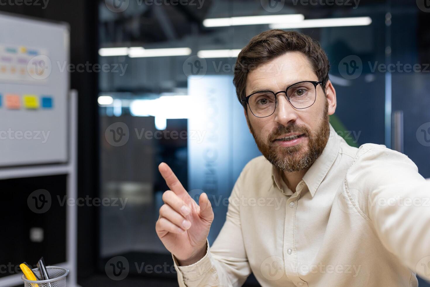 Close-up portrait of a young businessman in the office, pointing to an empty place, talking to the camera. photo