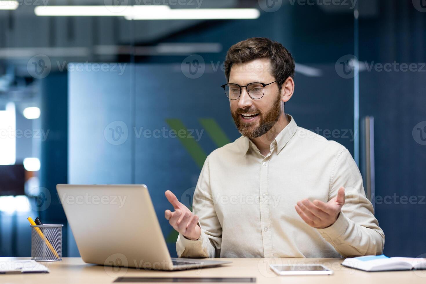A young successful businessman man is sitting in the office at the work table and is drawing on the conference online, gesturing with his hands. photo