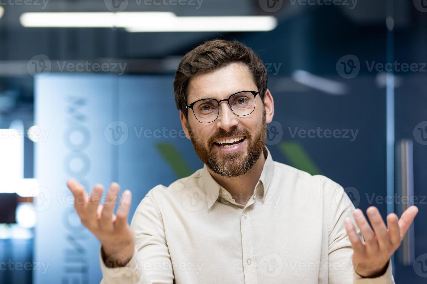 Close-up portrait of a young man sitting in an office at a desk, talking and gesturing to the camera. photo