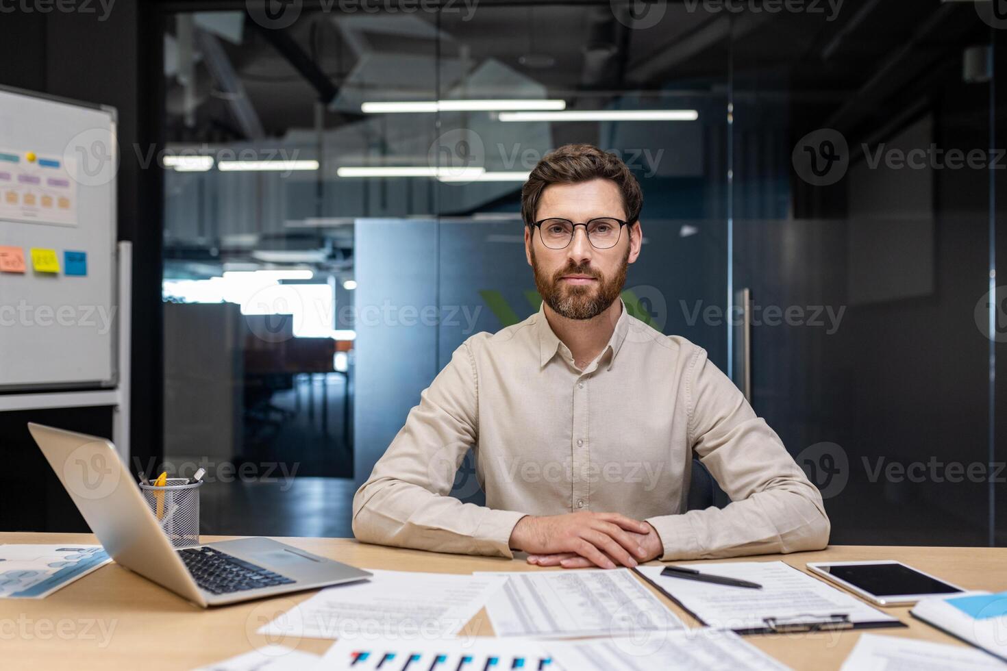 Portrait of a young serious and self-confident man sitting in the office at a desk behind a laptop and working with a project and documents. photo