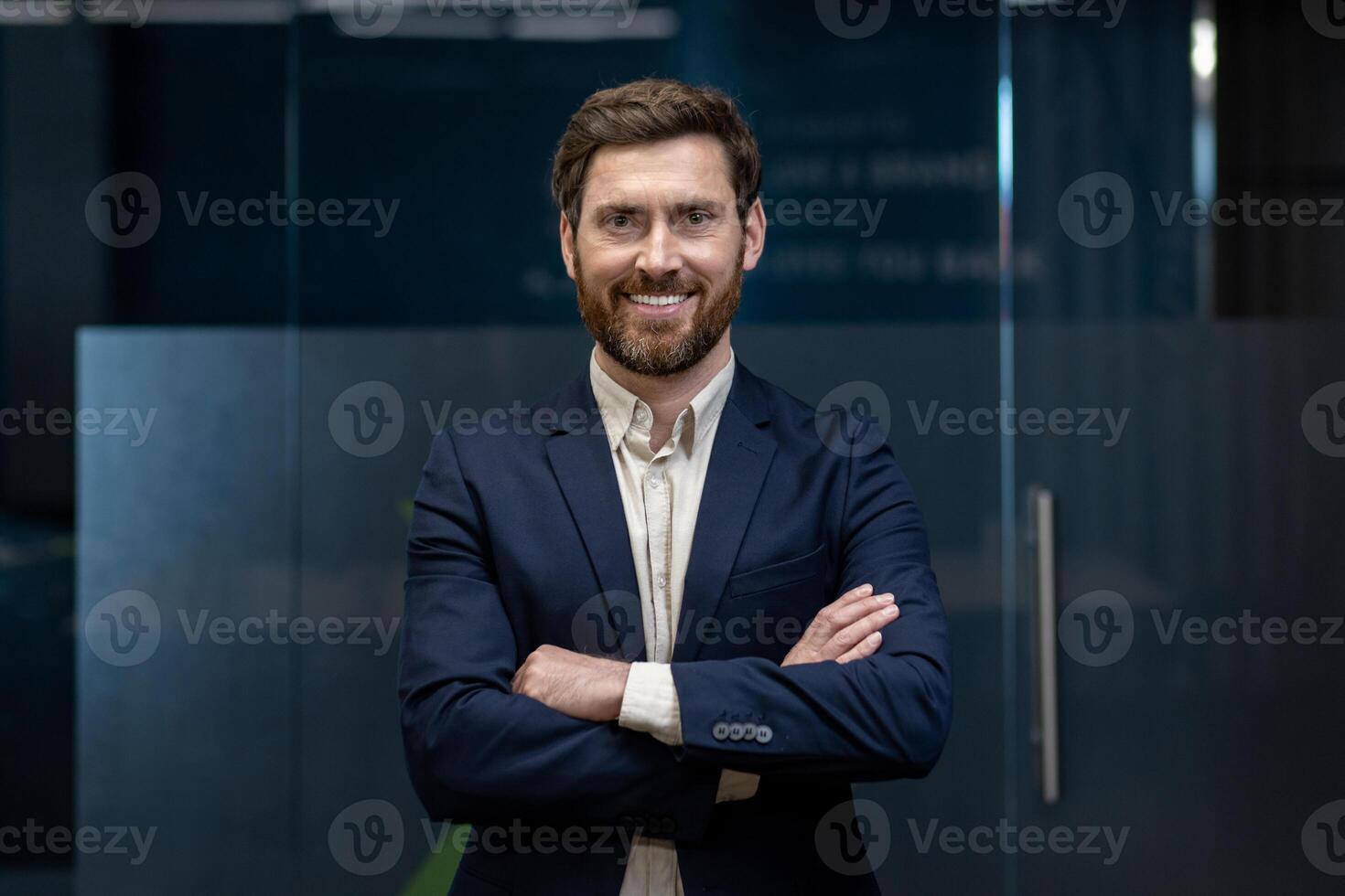Portrait of a sleepy young businessman standing in the office, arms crossed on his chest, confidently and smilingly looking at the camera. photo