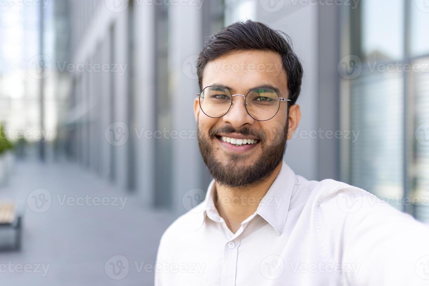 A smiling man with a beard and glasses poses in front of a modern building, offering a friendly and approachable presence. photo