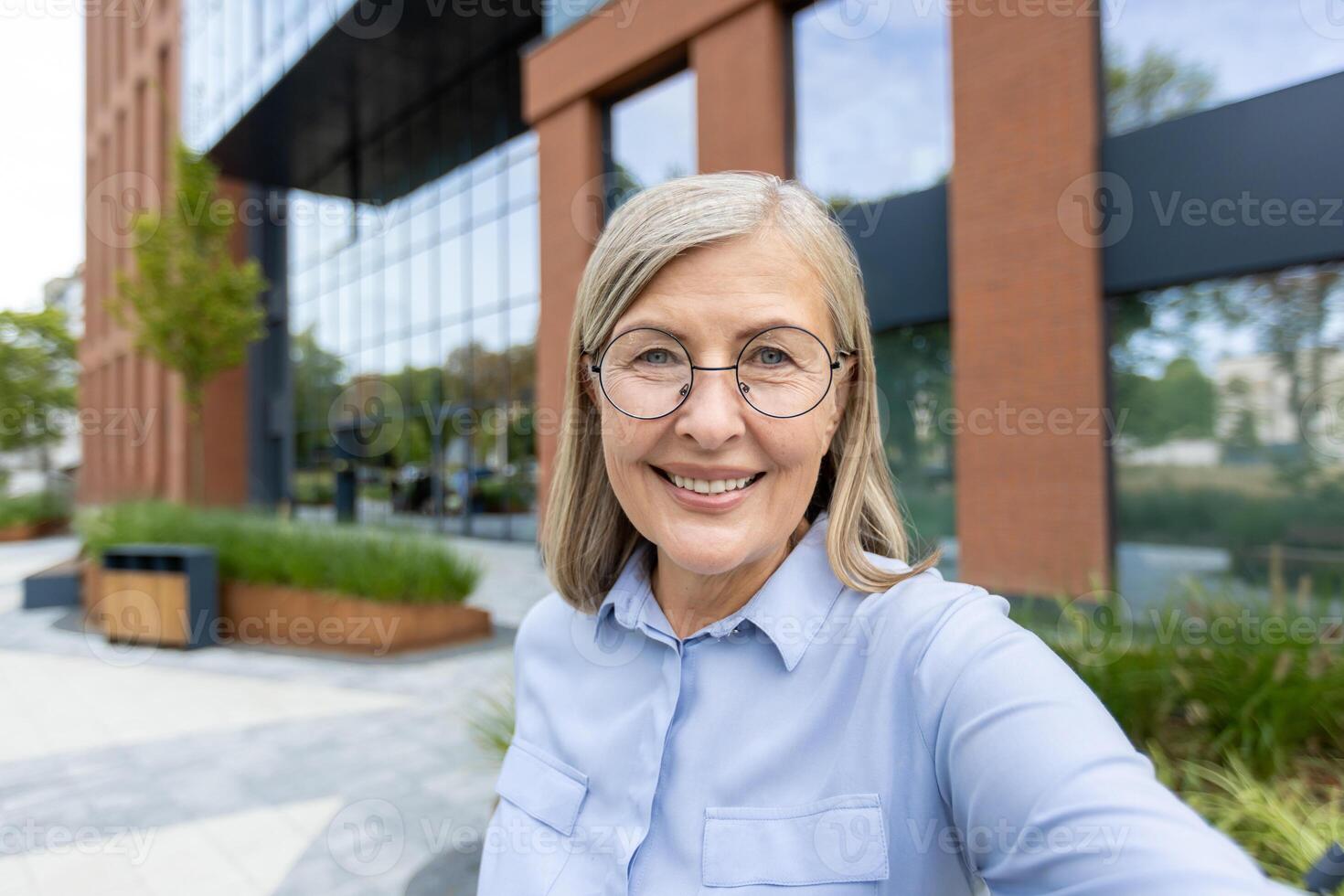 A businesswoman takes a selfie near her office building, capturing her radiant smile and the professional environment. photo