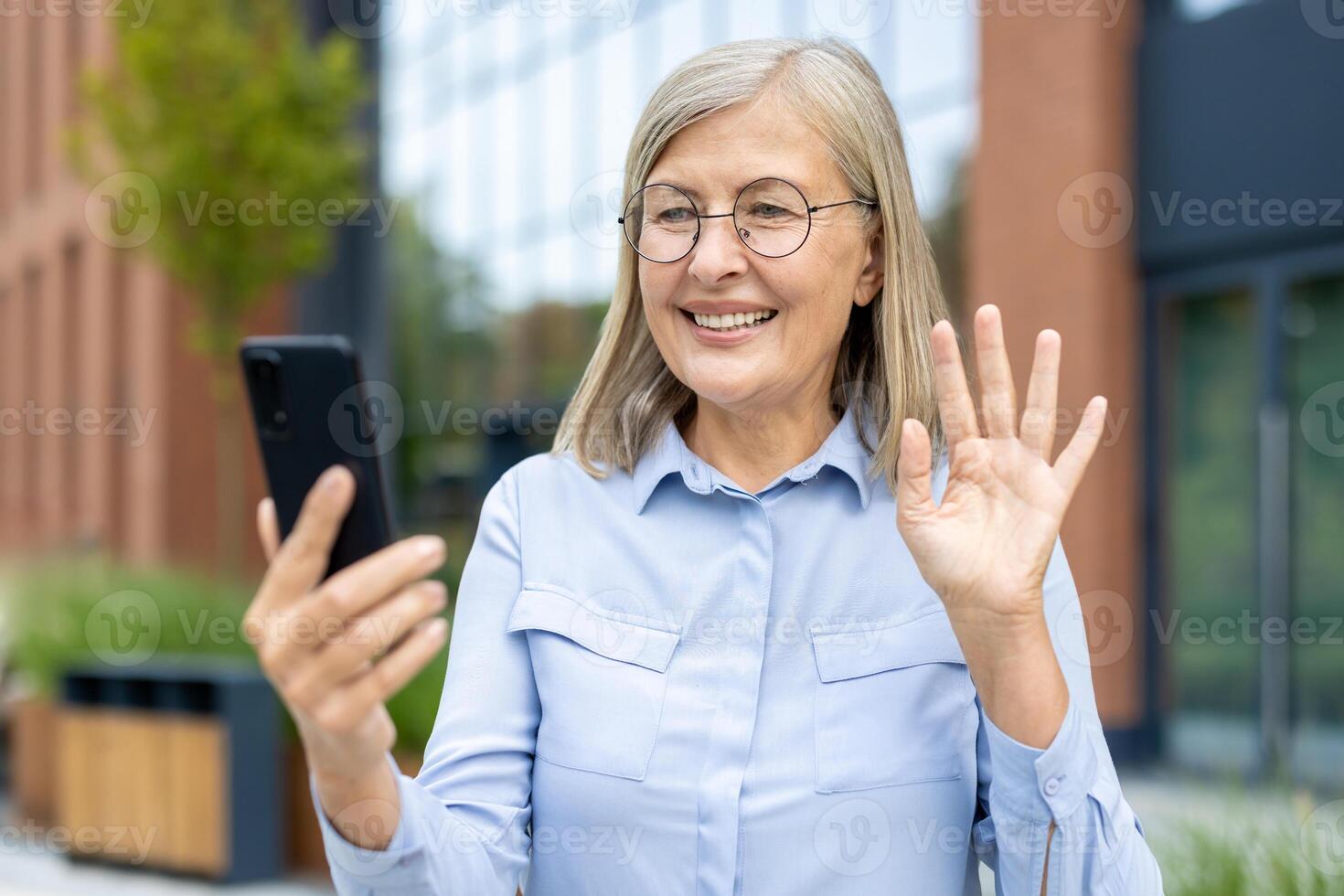 Smiling mature woman with glasses waving during a call using a smartphone, connecting with family and friends online. photo