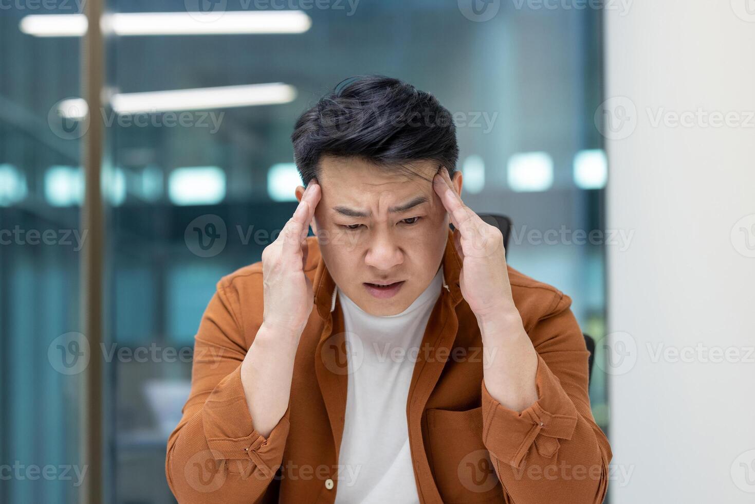 Headache in office worker at workplace. Man suffering from migraine while working inside office. photo
