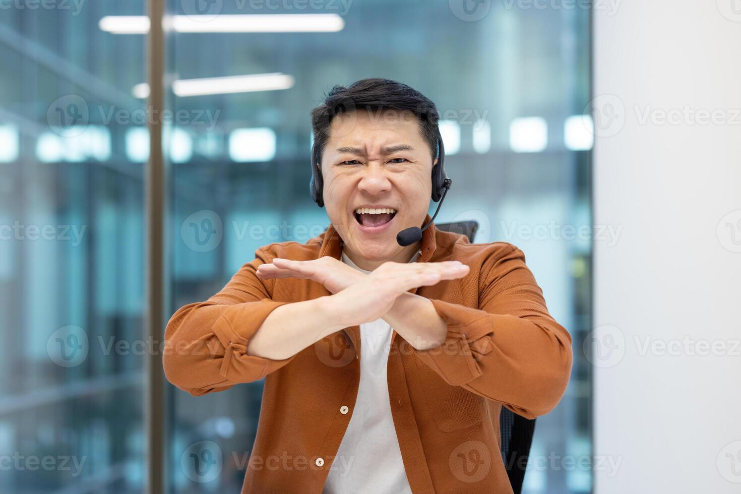 Webcam view, Asian man with headset quarreling angry shouting at camera. Dissatisfied support worker can't understand client. Man at workplace inside office. photo