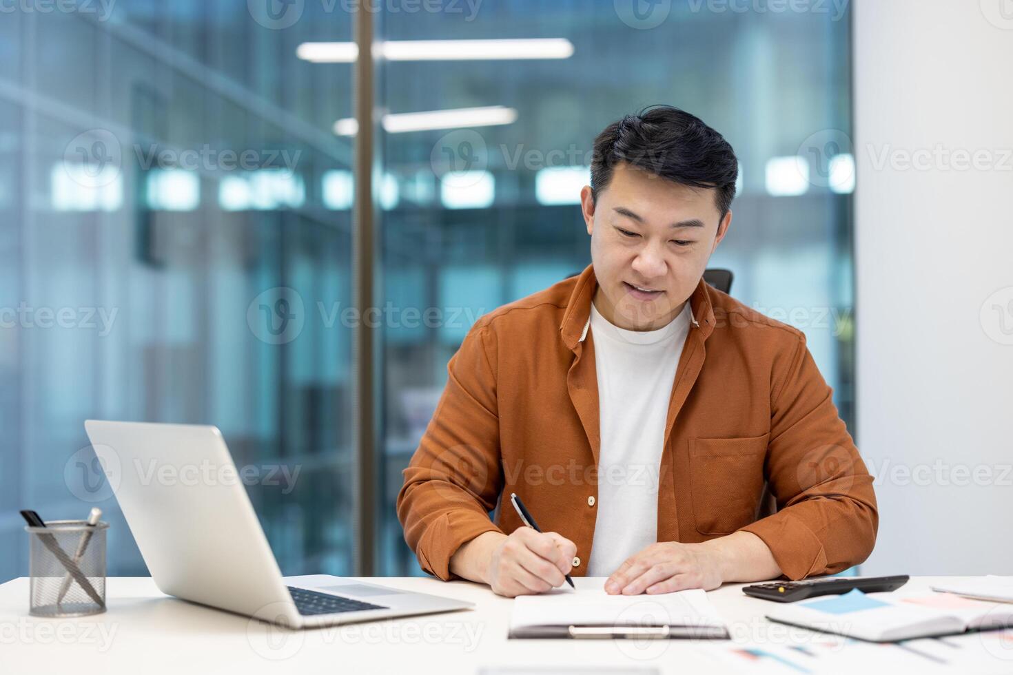 Successful financier accountant doing paperwork, asian man smiling filling out tax forms, preparing report. Businessman inside office among documents and bills inside office. photo
