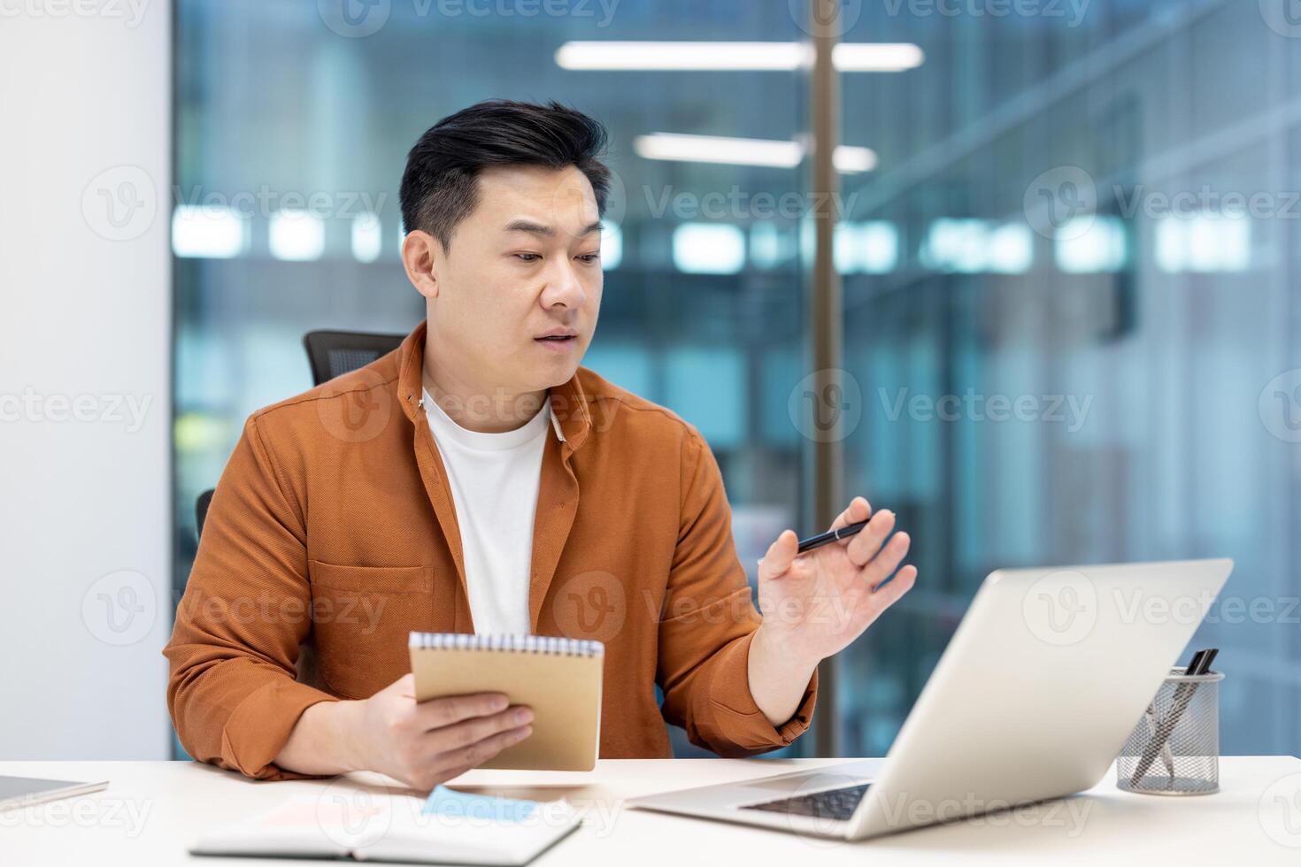 Successful businessman watching training webinar, man at workplace inside office writing data in notebook, asian man using laptop for online conference meeting. photo