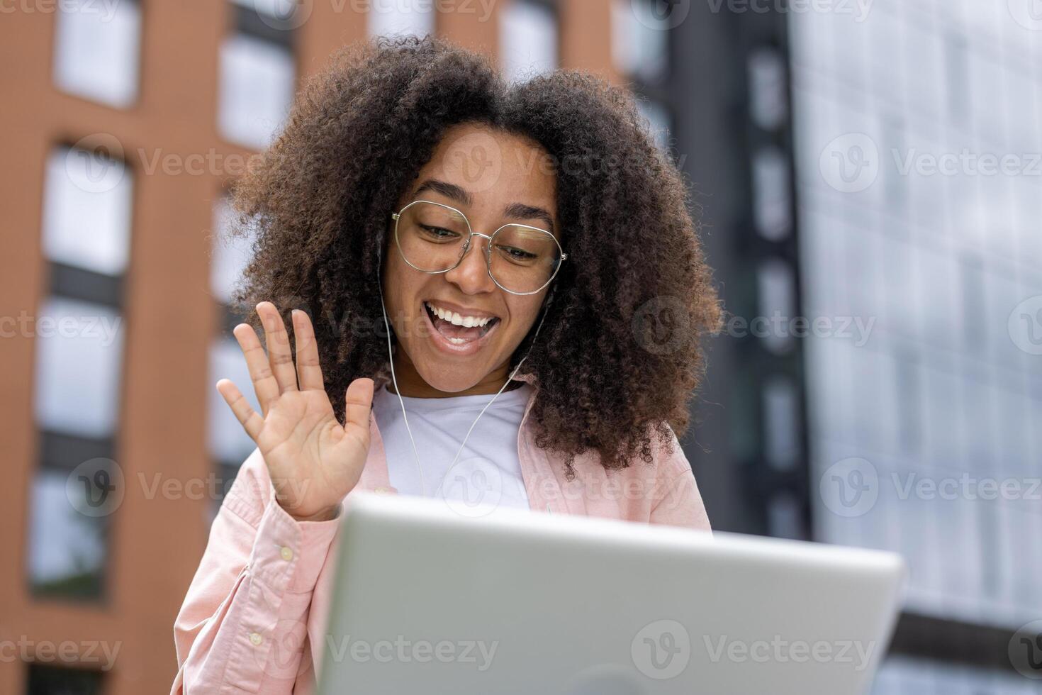 Smiling young woman engaged in a call, waving at her screen while sitting outside. Enjoying modern technology to stay connected with loved ones. photo