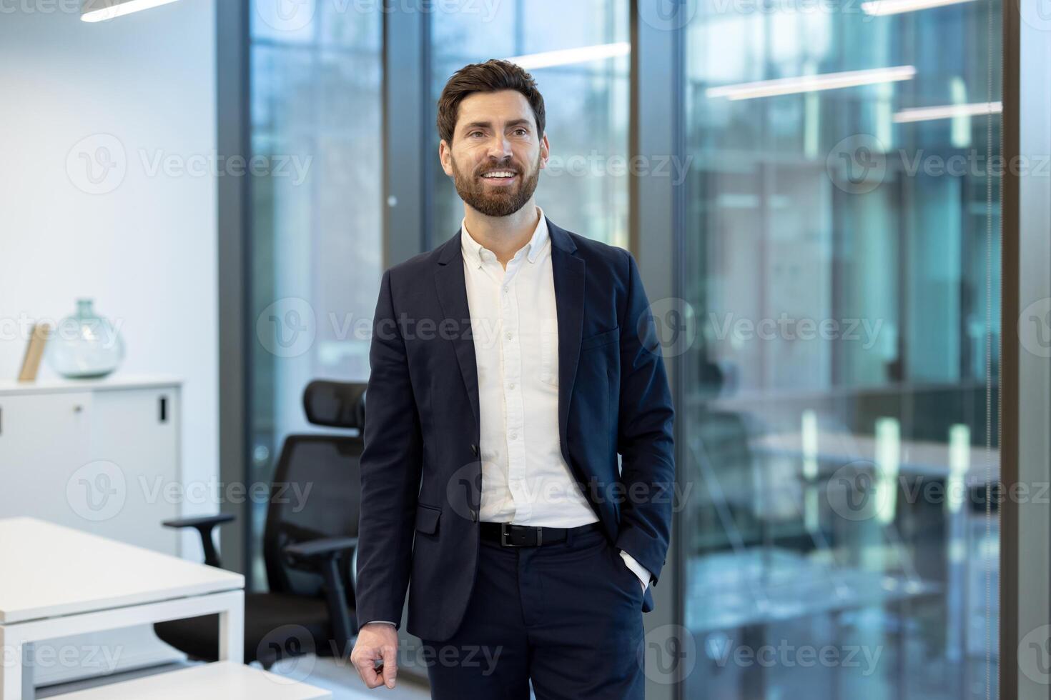 A smiling businessman stands confidently in a modern office setting, radiating success and professionalism. The natural light enhances the bright, contemporary design. photo