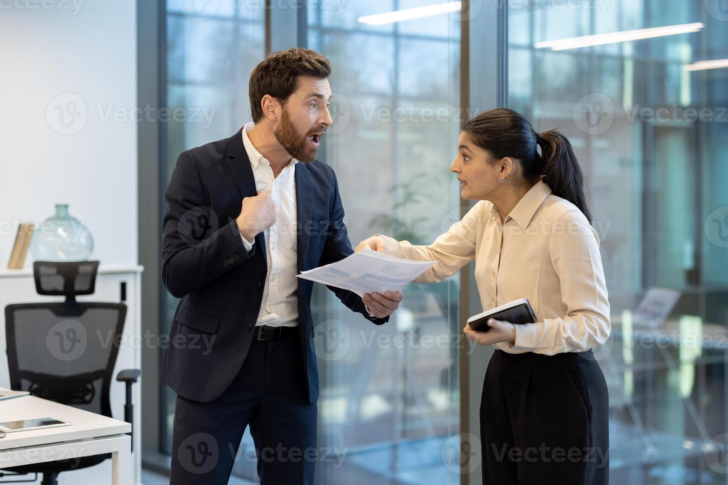 A man and woman are having a heated argument in the office while holding documents, showcasing workplace conflict photo