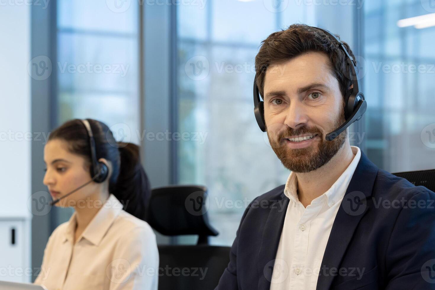 Two friendly professionals are ready to assist customers a man in focus smiles, while a woman works attentively in the background. photo