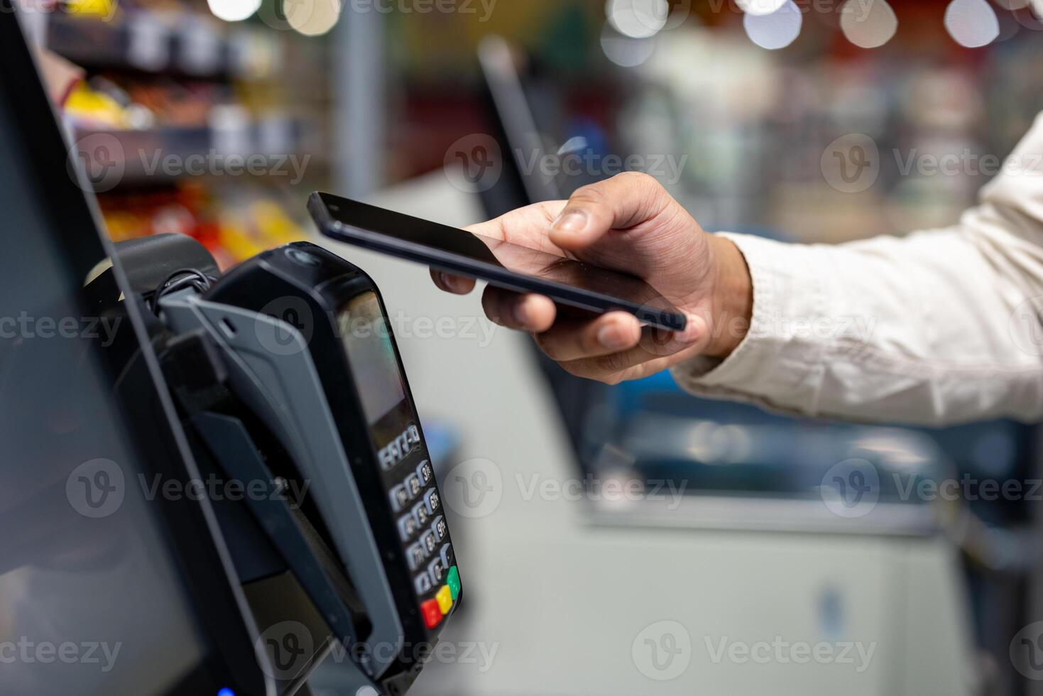 A person using a smartphone to make a contactless payment at a payment terminal in a store. It is a close-up shot. photo